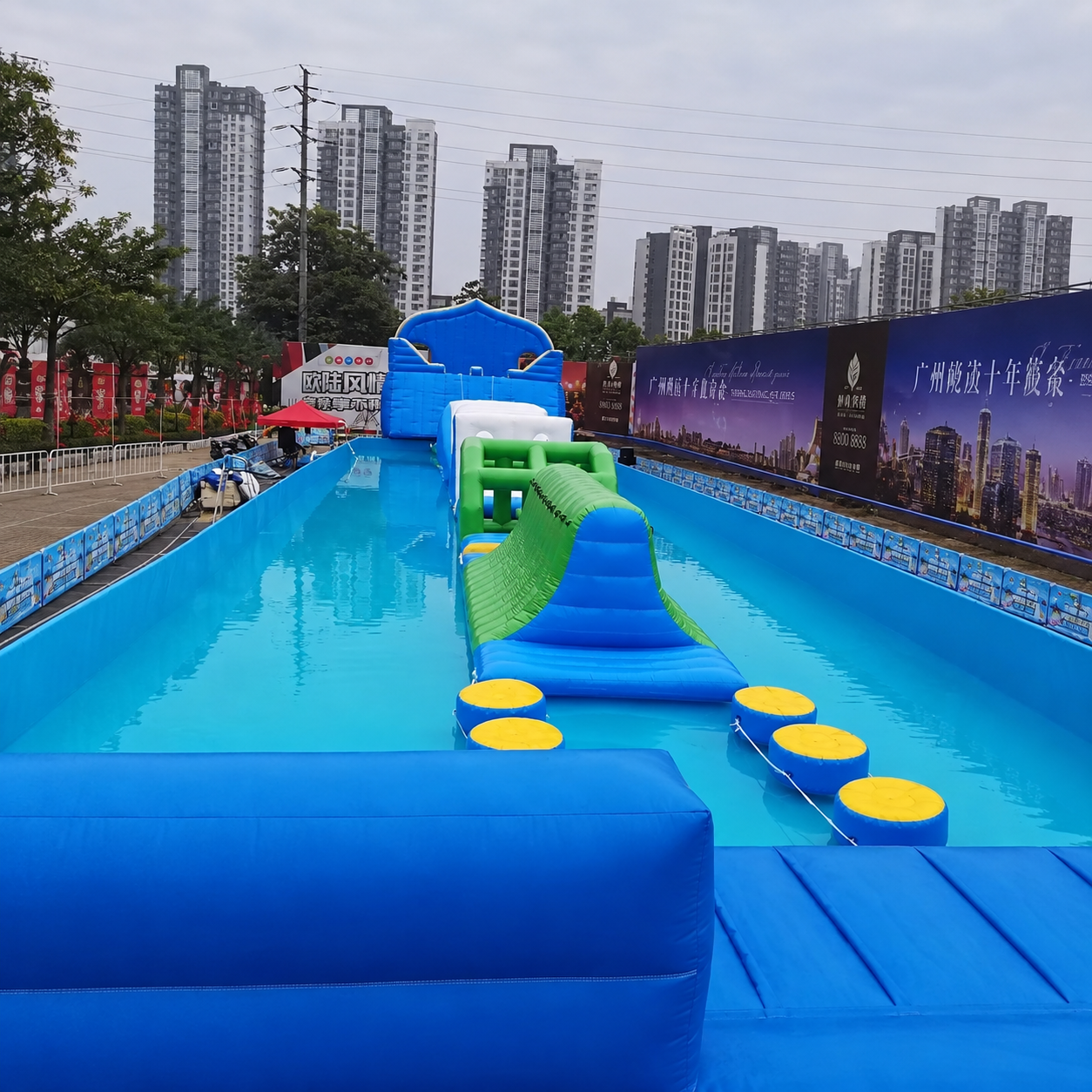 Blue and green inflatable obstacle course with yellow stepping pads in a long pool