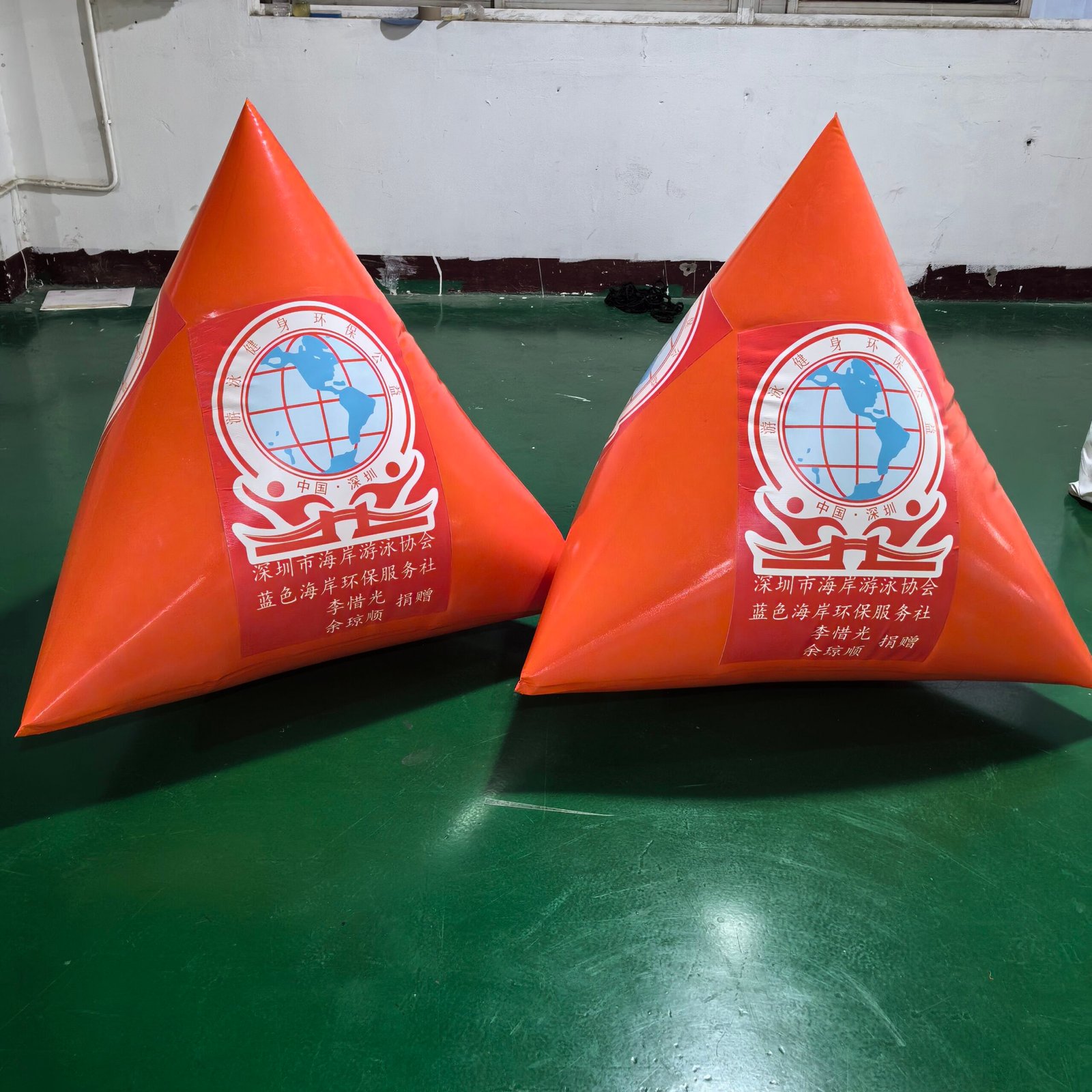 Two orange triangular inflatable marker buoys with printed logos