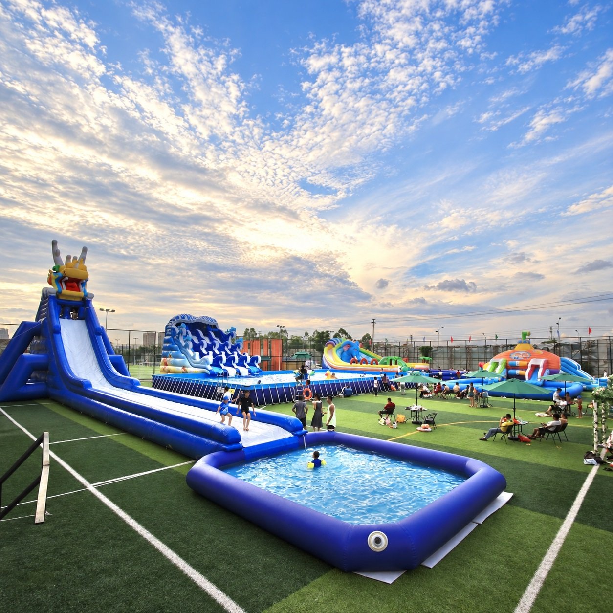 Blue inflatable water slide leading into a rectangular splash pool at sunset