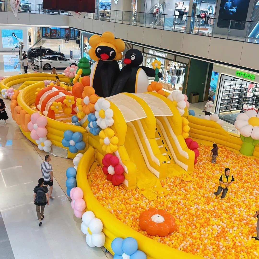 Yellow inflatable slide with penguin decorations leading into a ball pit